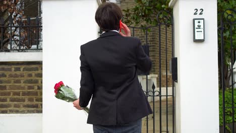 Hombre-Esperando-Frente-A-Una-Puerta-Con-Un-Ramo-De-Rosas-En-Las-Manos,-Haciendo-Una-Llamada-Pero-Nadie-Responde-Y-Nadie-Abre-La-Puerta