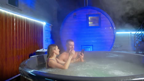 man and woman sitting in jacuzzi hold a smartphone. girl dials a number and man takes phone to the ear.