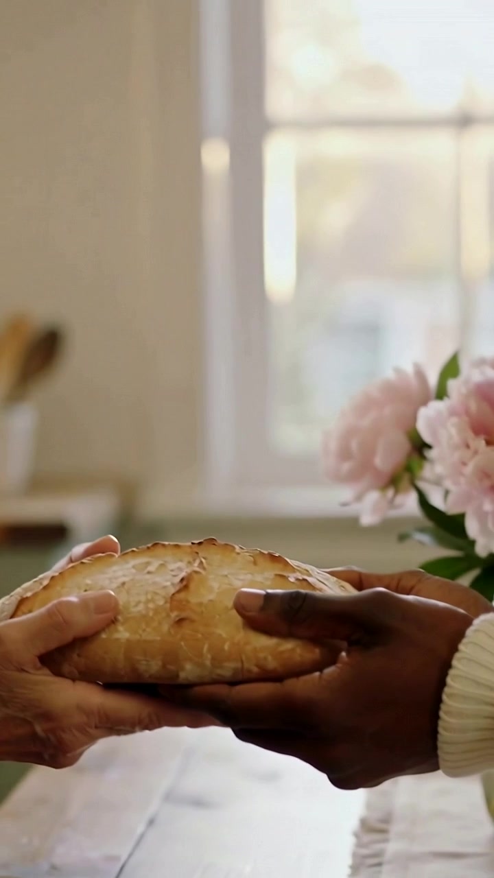 Vertical video: Two adults passing round loaf at table as right hand reaching to share