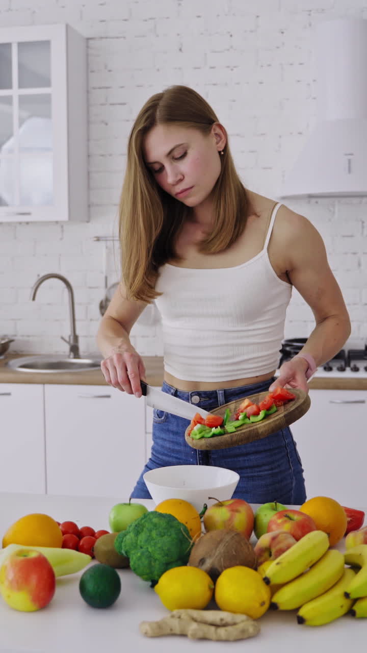 Young pretty woman preparing tasty salad on the modern kitchen. Lots of fresh organic ingredients on the table indoors. Healthy food. Dieting concept. Vertical video