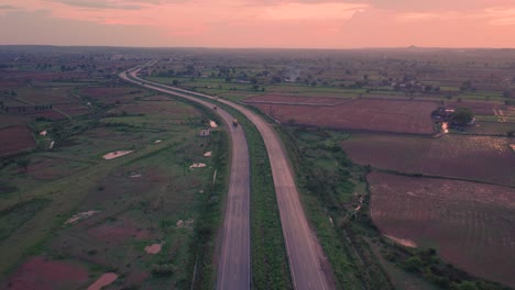 Luftdrohnenaufnahme-Einer-Autobahnstraße-Durch-Bauernhöfe-Im-Ländlichen-Gwalior-In-Indien-Bei-Sonnenuntergang-Mit-Wunderschönem-Orangefarbenen-Himmel-Und-Wolken-An-Der-Spitze