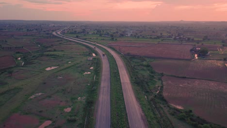 aerial drone shot of a highway road through farms in rural gwalior of india during sunset time with beautiful orange sky and clouds on top