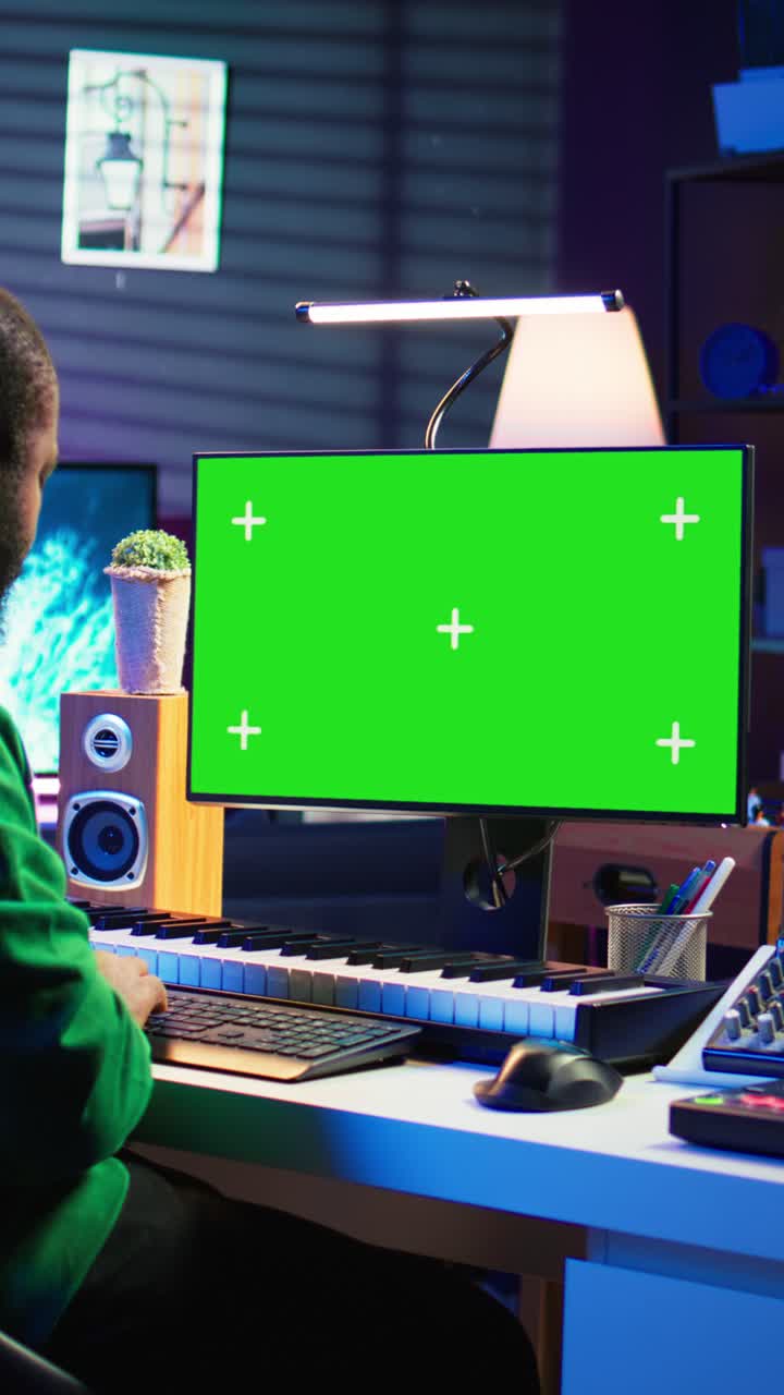 Produttore musicale che lavora al computer con green screen nello studio di casa