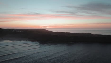 Antena:-Plataforma-Rodante-Lateral-Hacia-Los-Acantilados-Costeros-Con-Un-Telón-De-Fondo-Naranja-Del-Amanecer,-Rhossili-Gower,-Dron-4k