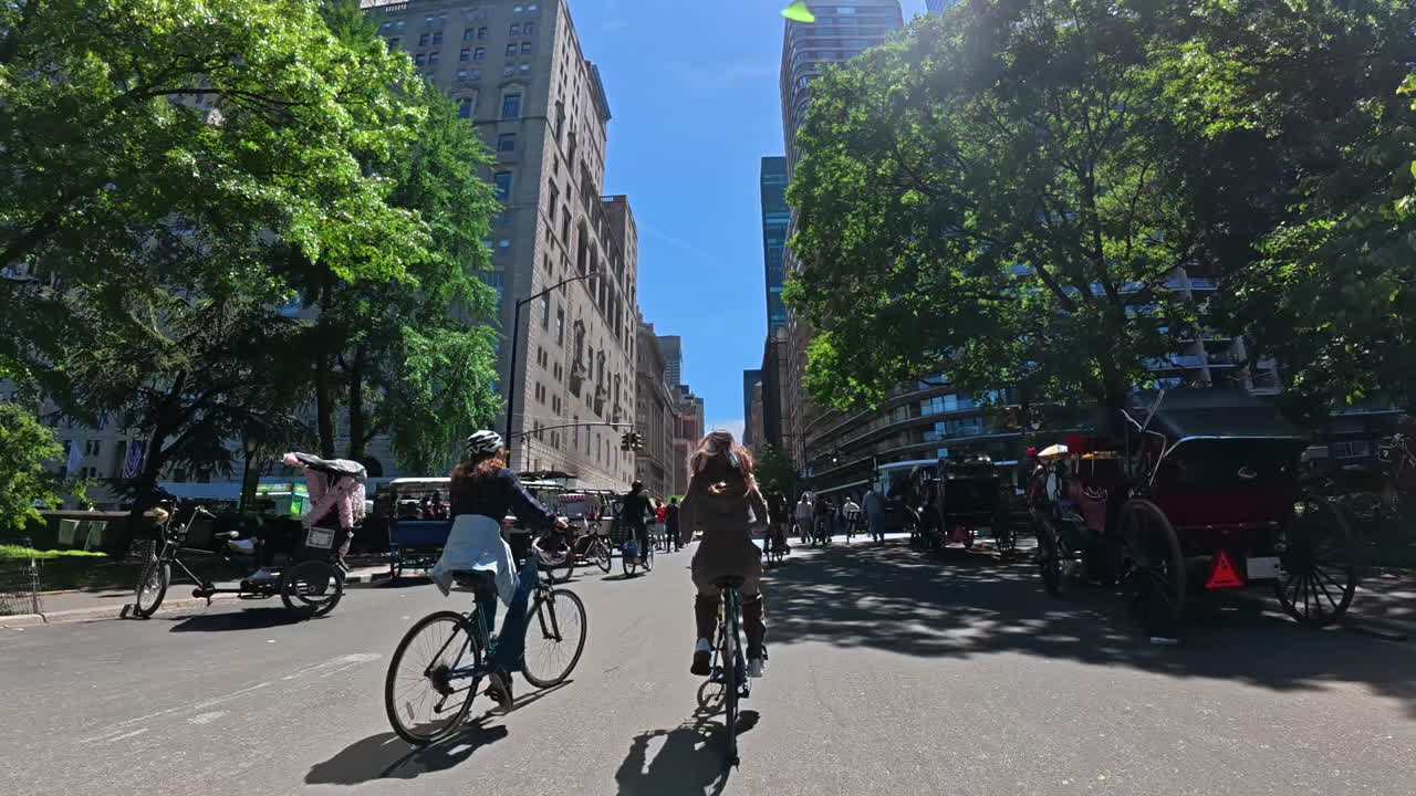 Nueva York, EE. UU., 1 de agosto de 2025: Ciclistas circulando por la carretera de Central Park. Los ciclistas pedalean por la carretera de Central Park con vegetación y edificios altos a lo lejos.