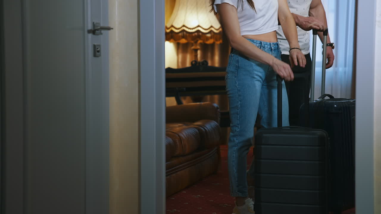 Couple with travel bags. Woman and man put their suitcases and sit on a sofa after the journey. Young couple arrives into the hotel. View from the door.