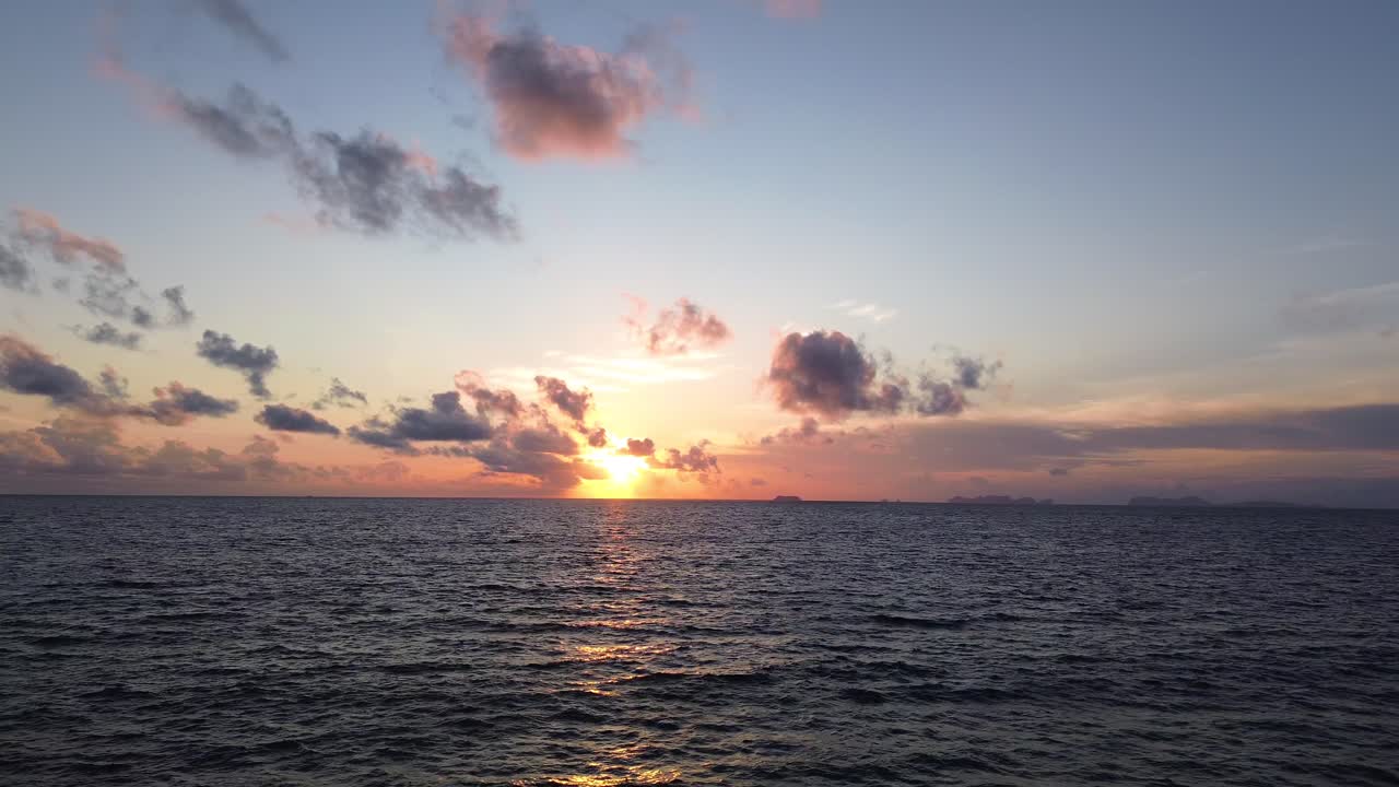 Aerial drone view of a glowing sunset above the open Andaman Sea near Koh Lanta, Thailand, with colorful clouds and distant islands stretching across the horizon