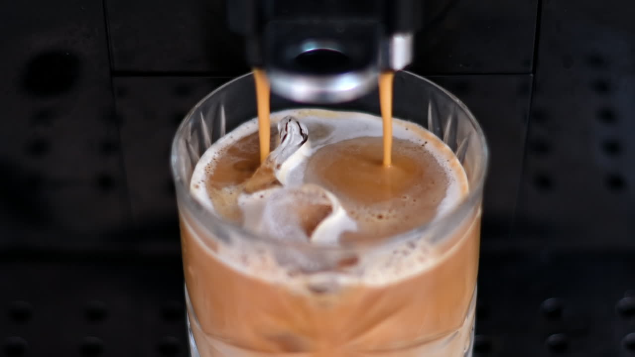 Close up of coffee pouring from a machine in a glass with ice