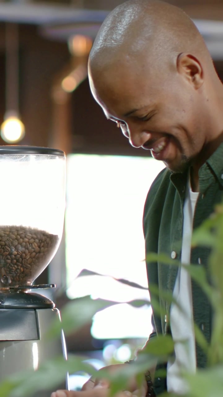 Video verticale: Uomo sorridente con una maglietta verde che posiziona una tazza sotto la tramoggia del macinacaffè in un bar, mentre prepara il caffè.