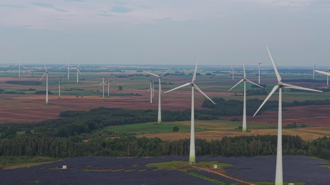Aerial view of multiple wind turbines spinning across vast farmland with a solar farm in the foreground, highlighting a sustainable energy landscape in the countryside