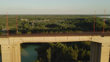 Dolly-right-flying-alongside-road-and-railway-complex-cable-stayed-bridge-with-large-green-field,-forest-area-and-river-at-golden-hour