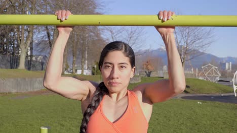 Closeup,-Young-Latina-Woman-doing-pullups-on-yellow-bar-outdoors