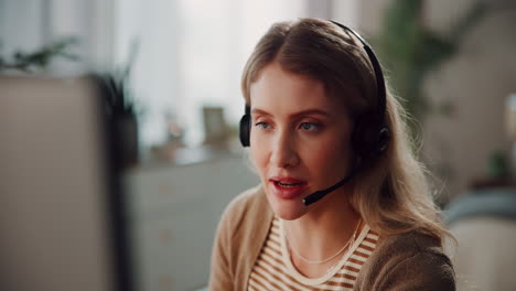 a young woman with blonde hair is on a call, wearing a headset and smiling while looking at a computer screen.