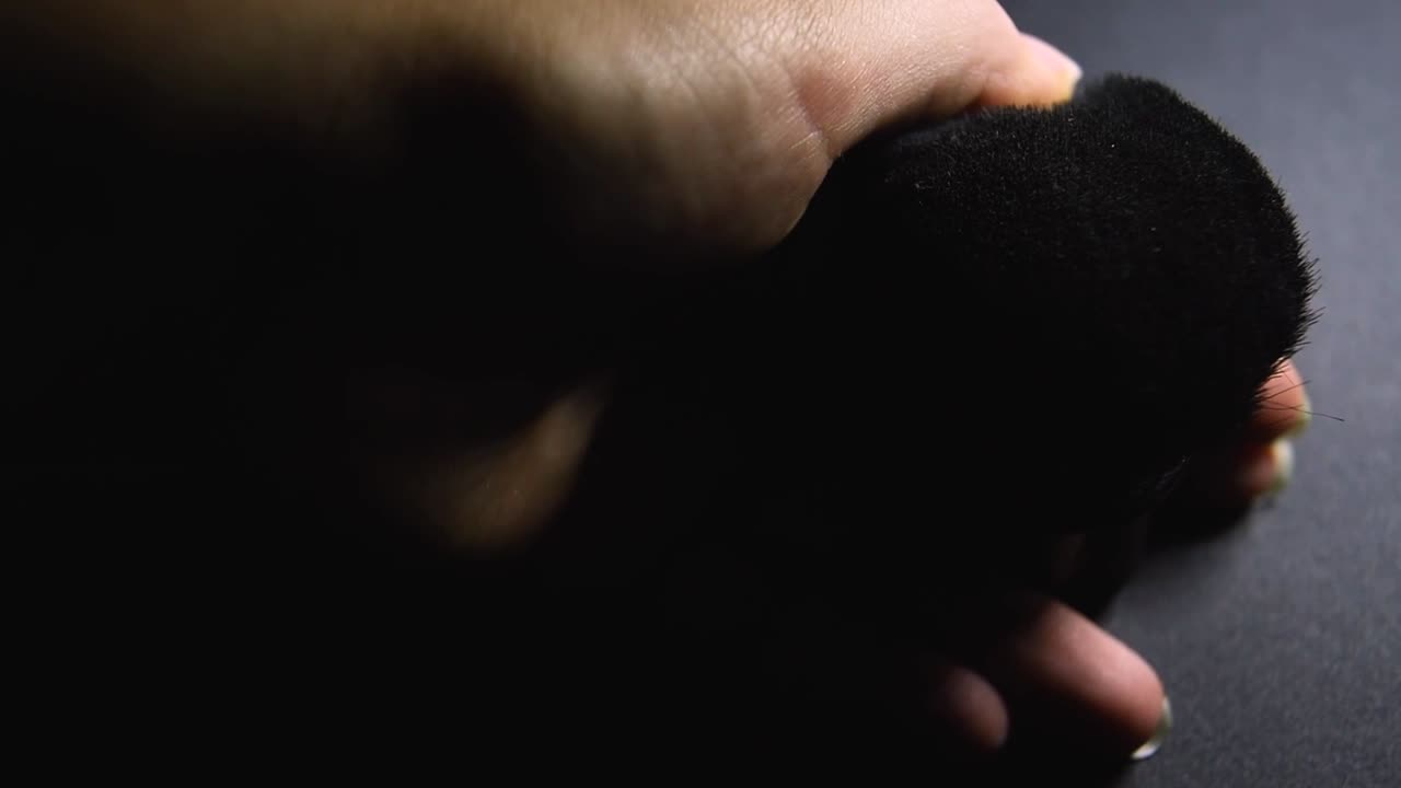 검은 backgorund에 크고 검은 메이크업 브러시를 만지고 청소하는 젊은 여성 손