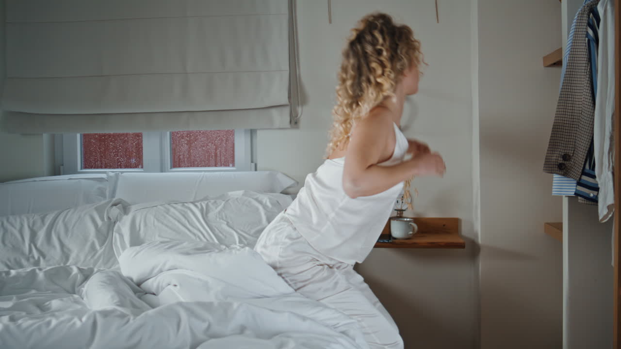 Relaxed woman waking bedroom sitting bed. Curly girl oversleep checking mobile