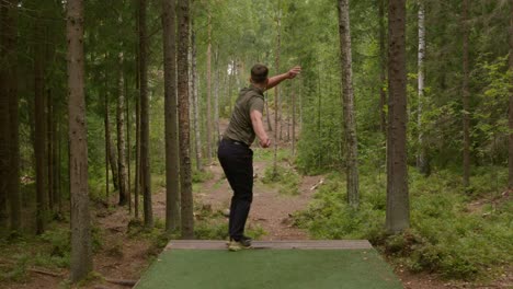 disc golfer lanza un tiro de apertura de revés desde el tee en un denso bosque finlandés