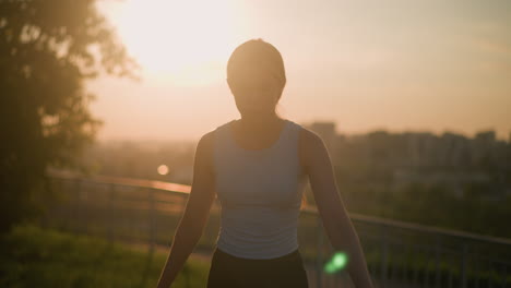 white lady roller skating outdoors under warm sunset glow, silhouetted against vibrant sunlight, with iron railing blurred behind her and distant cityscape