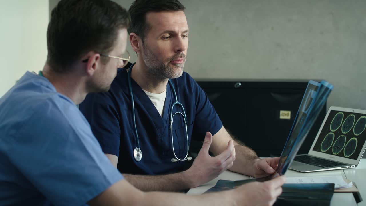 Vista laterale di due medici maschi caucasici che discutono una lastra radiografica su un pannello.