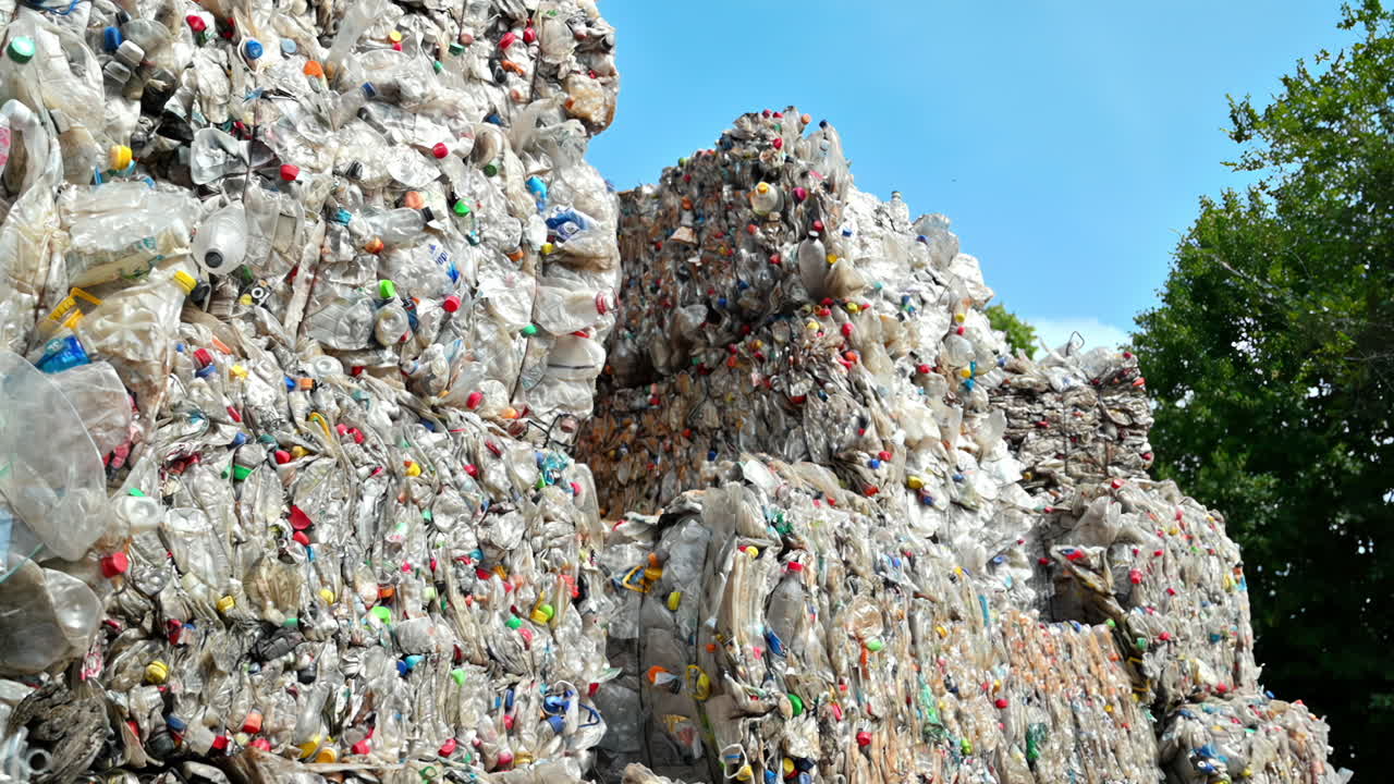 Multiple stacks of compressed transparent plastic garbage at waste recycling factory in open air. Slow motion