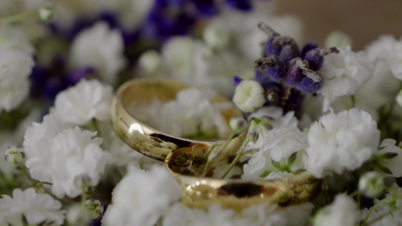 Close-up of golden wedding rings resting on a bouquet of white and purple flowers