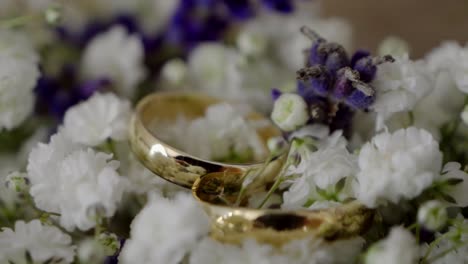 primer plano de anillos de bodas dorados descansando en un ramo de flores blancas y púrpuras
