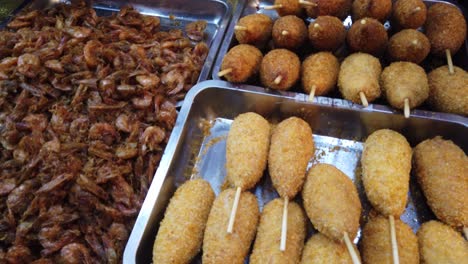 alimentos fritos callejeros indonesios expuestos en el mercado, mariscos y palitos de carne