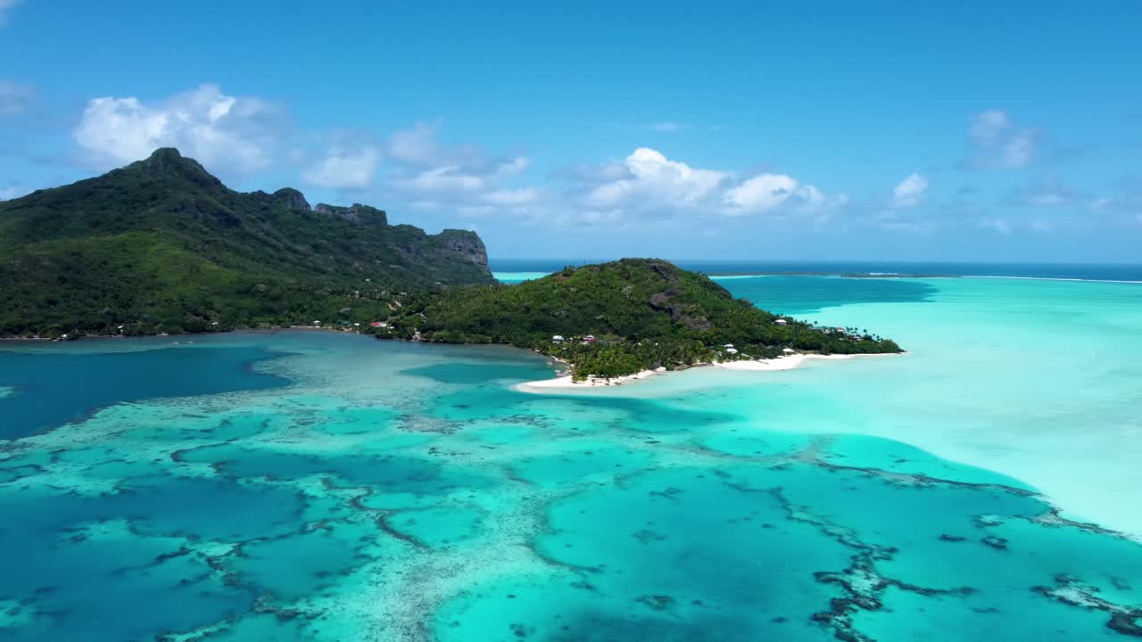 Drone view of a small green pacific tropical island with a lagoon, coral reef, white sand beach and blue shallow water on a sunny day in Maupiti, French Polynesia.