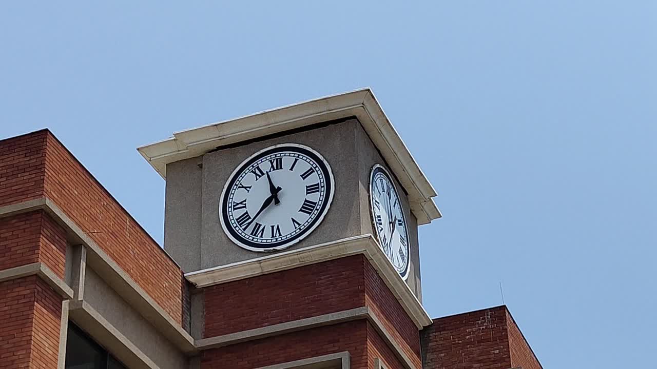 Static shot of classic clock tower with Roman numerals under clear sky in Vadodara, India. Ideal for time concepts, education, architecture and urban storytelling.
