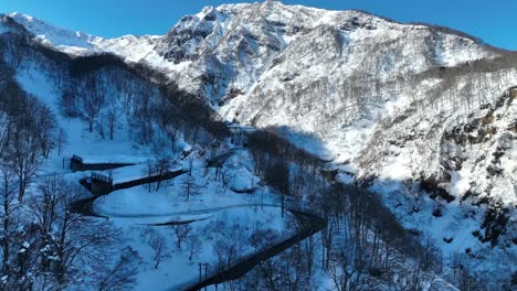 Drone-shot-flying-above-winding-road-at-base-of-massive-mountain-range