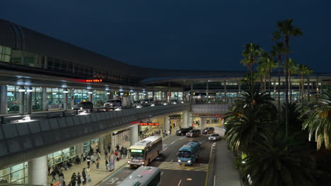 buses and cars driving at night with passengers waiting at the drop-off and pick-up point of jeju international airport in south korea