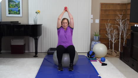 Mujer-Madura-Entrenando-Con-Mancuernas-Trabajando-Tríceps-Mientras-Se-Sienta-En-La-Pelota-De-Estabilidad-En-Casa