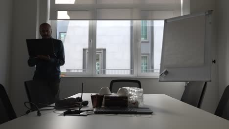 Bald-UK-Asian-Entrepreneur-Holding-Laptop-And-Pacing-Up-And-Down-Beside-Office-Room-Window