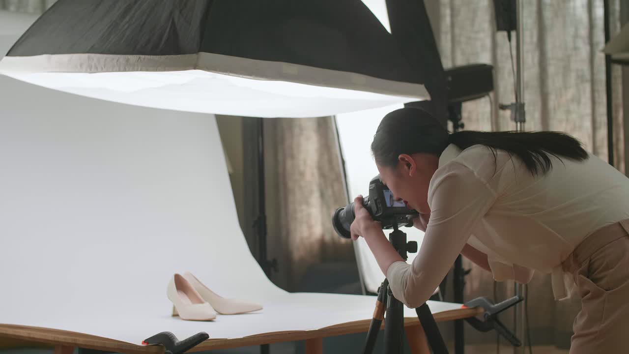 una fotógrafa asiática está cansada tomando fotos de zapatos de mujeres en su estudio casero.