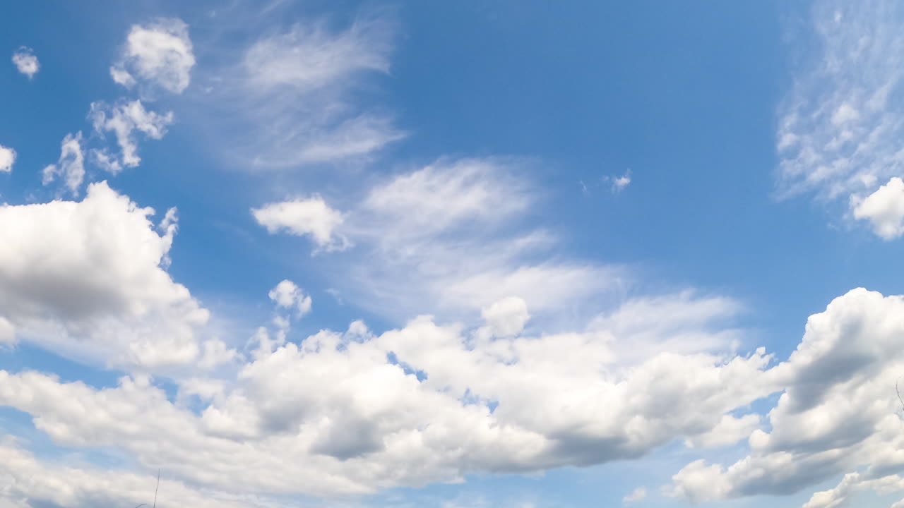 Cumulus and cirrus clouds in the blue sky. White cloudscape in the bright light of the summer sun. Timelapse.