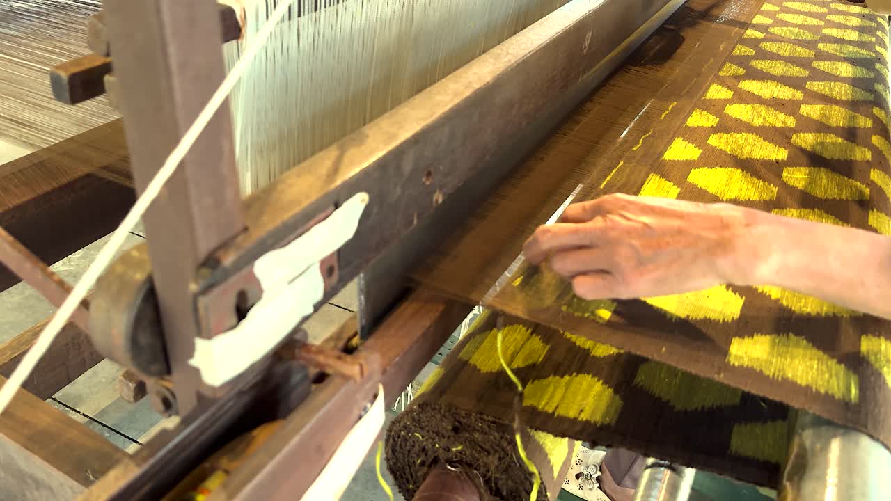Hands weaving intricate yellow silk patterns
