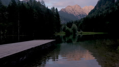 alpine mountain lake at sunset, plansar or plansarsko jezero in jezersko, slovenia, wooden pier extending above the water, kamnik savinja alps reflect in water with ripples