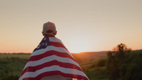 a man with an american flag on his shoulders against the backdrop of a picturesque valley where the sun sets