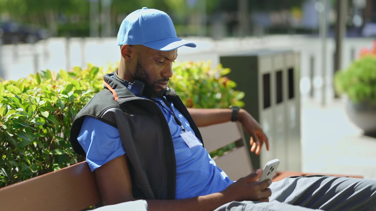 Delivery Worker Resting on Park Bench Using Smartphone