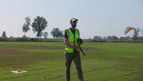 a man in a safety vest is getting the drone ready for flight on the school grounds - slow motion