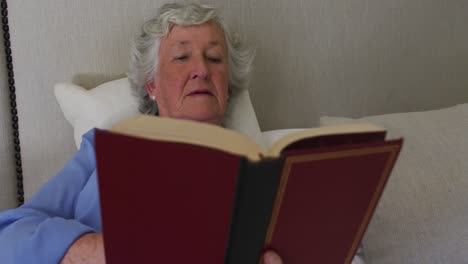 Glückliche-Kaukasische-ältere-Frau-Zu-Hause,-Die-Es-Genießt,-Im-Bett-Sitzend-Ein-Buch-Zu-Lesen