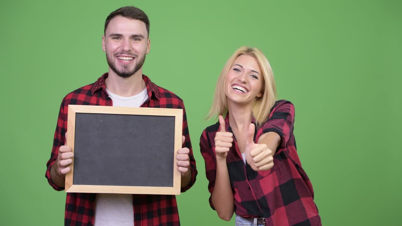 Young couple holding blackboard and giving thumbs up together