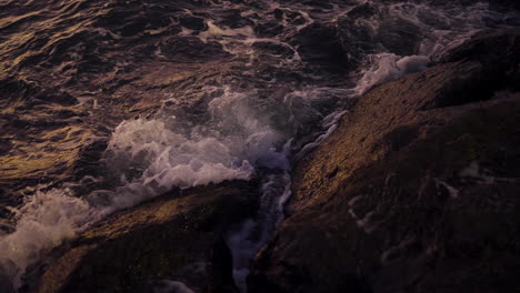 slow motion of waves splashing over rocks at dusk, capturing glistening reflections in coastal setting