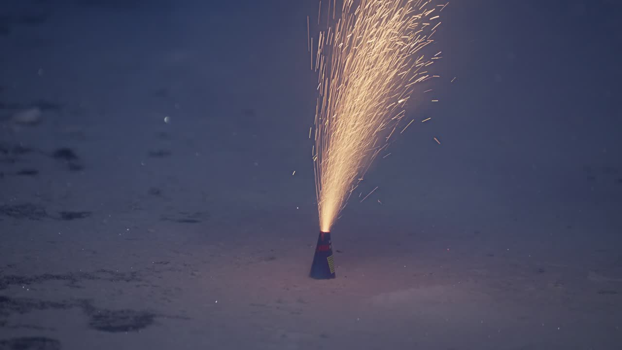 Un uomo accende un fiammifero per illuminare un piccolo fuoco d'artificio a forma di cono sulla neve, si allontana mentre scintille e fiamme si alzano, per poi spegnersi