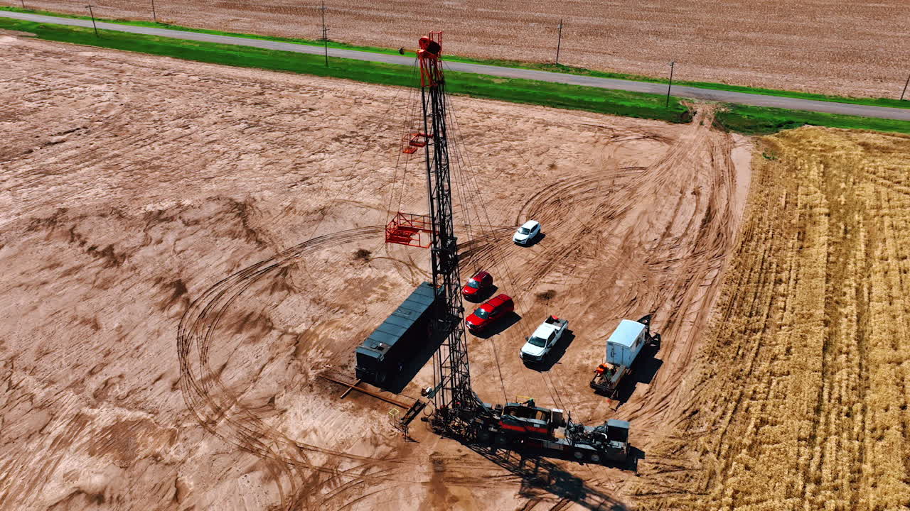 Location in the bare field with a little site for oil production. Truck with a tower and few cars around from aerial perspective.