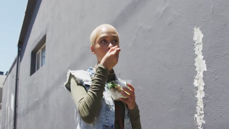 Mixed-race-woman-walking-on-street-and-eating-a-takeaway-salad-lunch-