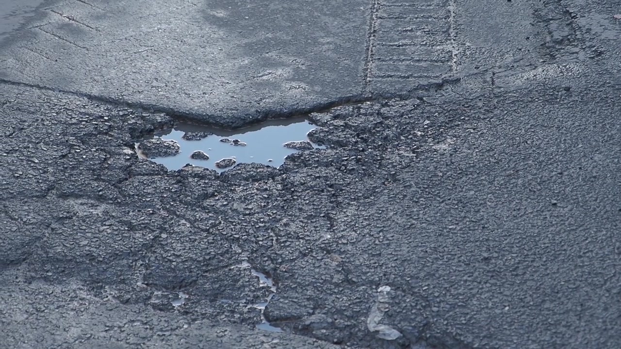 Lähikuva asfalttitiellä olevasta vedellä täytetystä kuopasta