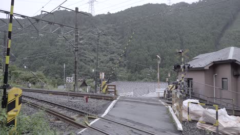 closing bars at railway crossing in rural area with house and forest in distance - locked off view