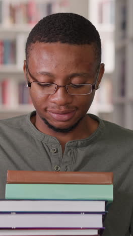 black teacher with book stack in library. african american man carries high textbooks heap along aisle between information archive. school education