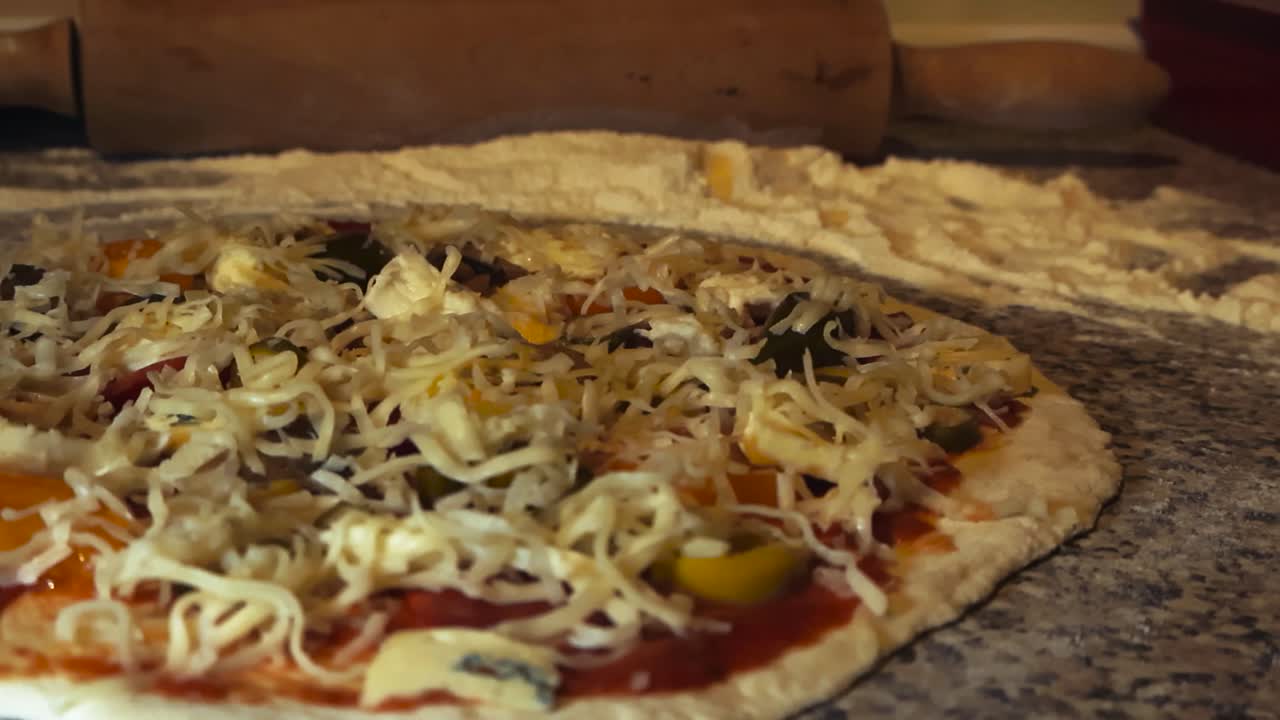 Raw white and fluffy delicious pizza dough on a home kitchen flour covered table with toppings on the pizza like cheese, jalapenos, minced meat and tomato sauce. rolling pin in the blurry background
