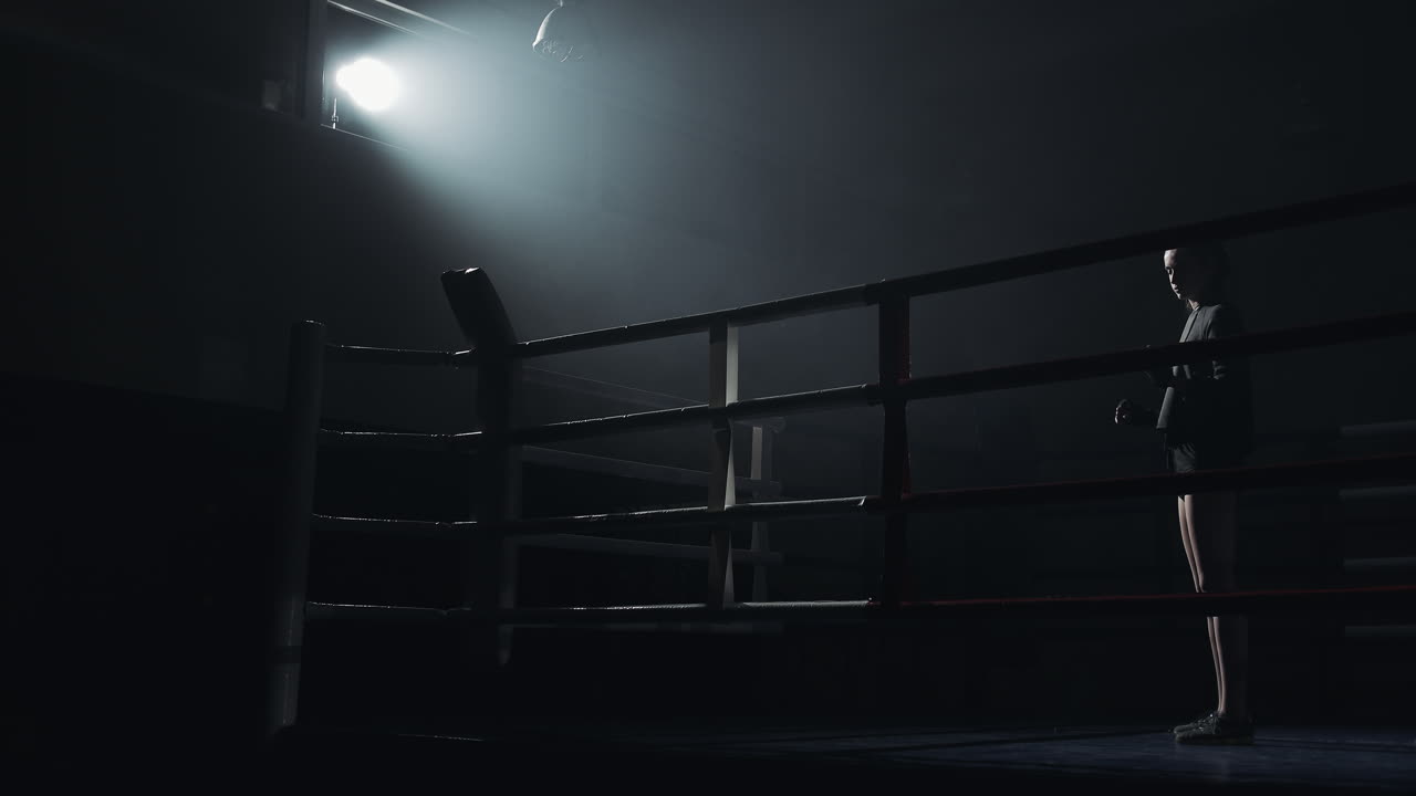 A boxer stands in a dimly lit boxing ring under a spotlight